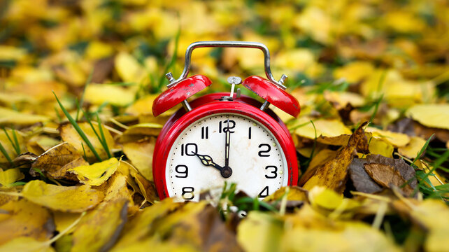 Retro alarm clock in the golden autumn fall leaves, daylight savings time banner or background