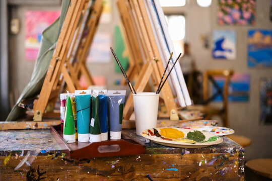 Acrylic paints tubes, pallets and wooden easels on table in art class or artist studio workplace