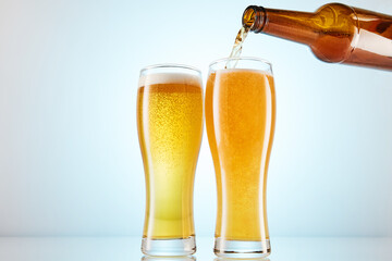 Lager, ale flows to empty tall glasses from bottle.