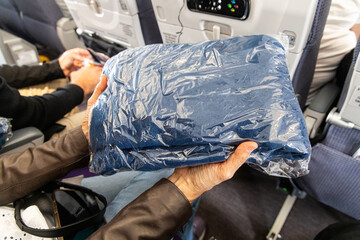 Passenger holding sanitized and sealed wool blanket in plastic bag provided to passengers to keep warm and comfortable during flight