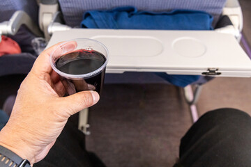 Passenger holding a glass of red wine, served as part of beverage selection during flight in airplane