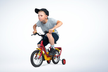 Fototapeta na wymiar A teenage boy in a cap, T-shirt and shorts rides a children's bike on light blue background. File contains a path to isolation.