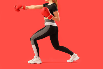 Fototapeta na wymiar Young woman in sportswear and boxing gloves on red background