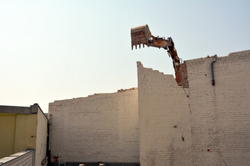 Demolition of a brick wall of an old building using an excavator bucket. Dismantling of the city's...
