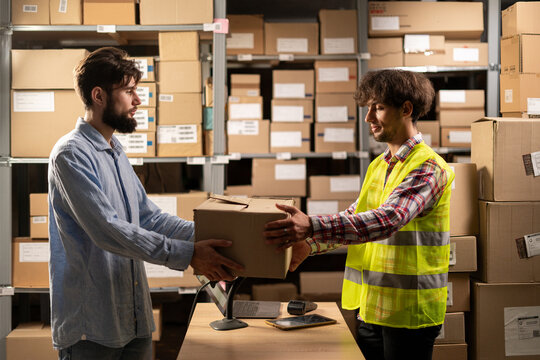 Male customer take online order at pick-up point. Online store warehouse worker giving parcel to man client at post office.