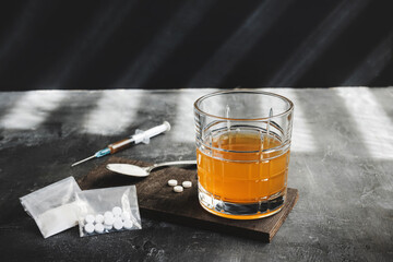 Alcohol drink in a glass, syringe with a dose of drugs, white pills and narcotics powder in a...