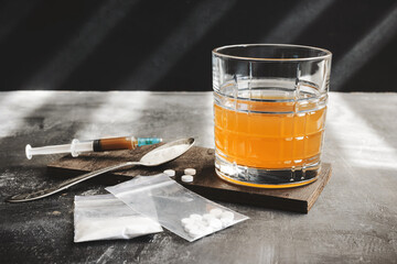 Alcohol drink in a glass, syringe with a dose of drugs, white pills and narcotics powder in a transparent bag on dark background. Concept of addiction, abuse and bad habits