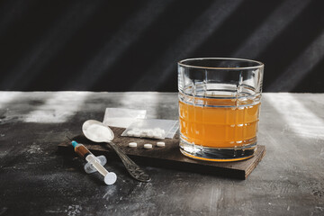 Alcohol drink in a glass, syringe with a dose of drugs, white pills and narcotics powder in a...