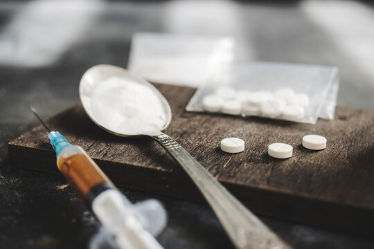 Syringe with a dose of drugs, white pills and narcotics powder in a spoon on dark background. Concept of addiction, abuse and bad habits