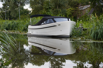 Small boat in ditch during sunset, surrounded by water lillies and reed.