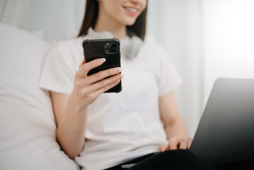 Beautiful young woman on a white bed with coffee cub and using smart phone at home. lifestyle concept.