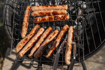 Closeup photo of sausages. Grilling chicken sausages outside on a barbecue grill. Grill tongs in a foreground. First outdoor grill party in the spring season. Healthy barbecue.