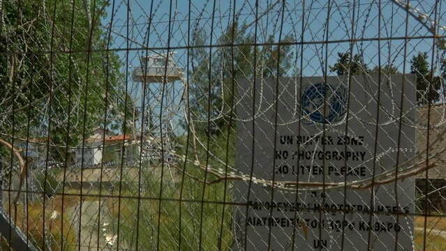 A 'UN' buffer zone sign, with: "no photography and no litter please" are written in the sign as well. a metal watch tower is visible in the background. Nicosia, Cyprus.