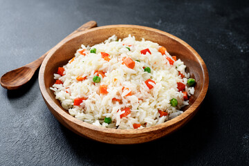 Wooden plate with vegetable fried rice - healthy vegetarian food. Dark background .
