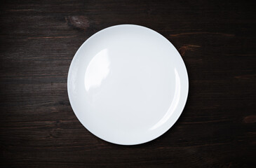 Blank white dish on dark wooden background. Flat lay.