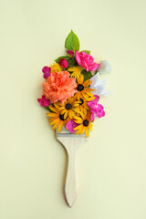 Brush with different colorful flowers on beige background, top view. Creative concept.	