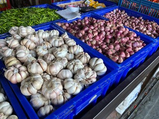 Pile of garlic and onion on a blue plastic tray being displayed in a traditional market for sale