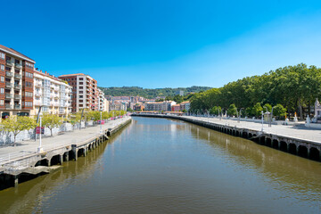 Obraz premium Bilbao, SPAIN - July 19 2022: Bilbao city center. View of Nervion River with promenade area. At the right Arenal Park. Bilbao is the largest city in the Basque Country, beautiful travel destination