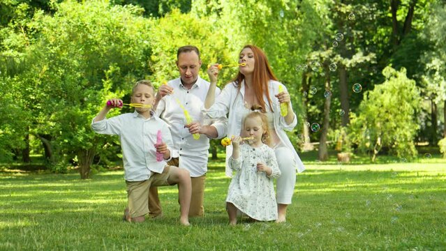 Family with two kids blowing bubbles together in park. Big family having fun outdoors. Happy family resting in summer park. Pregnant mother. 4K, UHD