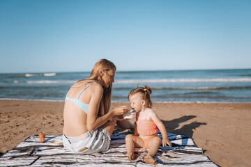 mom feeds her daughter on the beach. little child sea, girl in swimsuit joyful