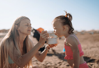 mom feeds her daughter on the beach. little child sea, girl in swimsuit joyful