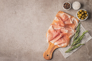Thin slices of Italian prosciutto with green olives, spices and rosemary on wooden cutting broad....