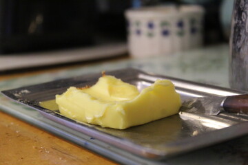 A close up photo of a slab of butter on a metal plate on a wooden counter.