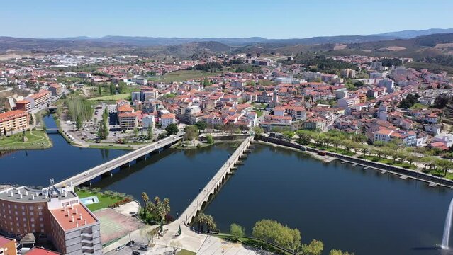 Scenic drone view of Mirandela, small Portuguese city on banks of Tua overlooking terracotta roofs of residential buildings and two bridges across river on sunny spring day