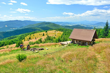 Fototapeta na wymiar Group of tourists relax, socialize and picnic on weekends at mountains meadow and wooden hut in summer sunny day, Mogielica, Island Beskids (Beskid Wyspowy), Poland