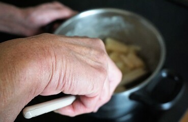 Alte Frauenhand rührt mit Kochlöffel Kohlrabi in Kochtopf um auf Herdplatte in Küche 
