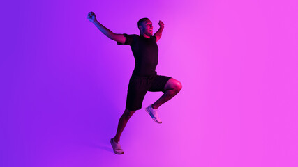 Fototapeta na wymiar Emotional black runner shaking fists running on purple neon background