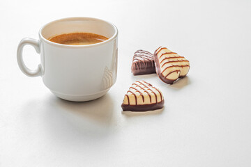 cup of coffee and gourmet heart shaped chocolate sweets on white surface