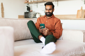 Middle Eastern Guy texting on smartphone and websurfing at home