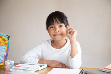 Cute kid drawing with water colour. Little girl writing something in copybook and sitting at table.