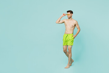 Full body side view young sexy man wear green shorts swimsuit sunglasses relax near hotel pool look...