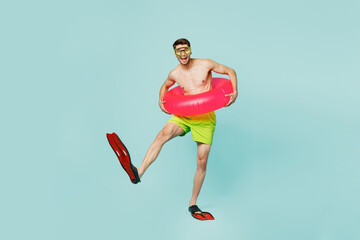 Full body satisfied young man wear green shorts swimsuit relax near hotel pool hold in hand inflatable rubber ring flippers isolated on plain blue background. Summer vacation sea rest sun tan concept. © ViDi Studio