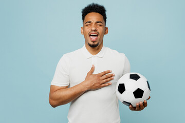 Young man fan wearing basic t-shirt sing national country anthem cheer up support football sport team holding in hand soccer ball watch tv live stream isolated on plain blue color background studio. - obrazy, fototapety, plakaty