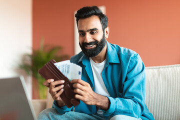 Joyful Middle Eastern Guy counting money in wallet at home