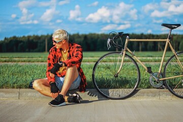 a cyclist in glasses and a red shirt sits on the side of the bike and rests