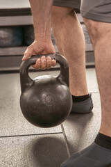 Naklejka na ściany i meble Man's hand lifts a metal kettlebell from the floor in the gym. Close-up