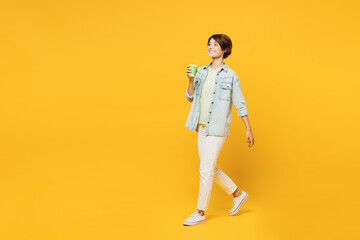 Full body young happy woman she wear green t-shirt denim shirt casual clothes hold takeaway delivery craft paper brown cup coffee to go isolated on plain yellow background studio. Lifestyle concept.