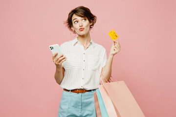 Young woman wear casual clothes hold paper package bags using mobile cell phone hold credit bank card shopping online isolated on plain pink color background studio. Black Friday sale buy day concept.
