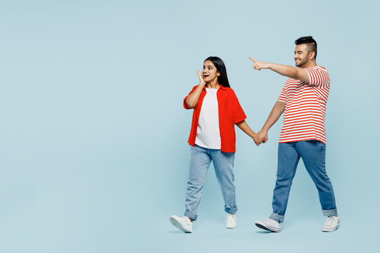 Full body young couple two friends family Indian man woman wear red casual clothes t-shirts together walk go point index finger aside on area isolated on pastel plain light blue cyan color background.