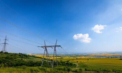 Fototapeta na wymiar Massive electric power pylons on a hill next to agriculture fields in central Bulgaria.