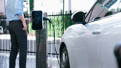 Progressive businessman install charger plug from charging station to his electric car before...