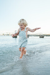 Adorable happy kid splashing in water of sea on coast