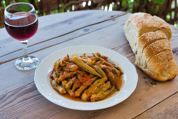 traditional Greek food for the summer, okra in a pot, with fresh tomatoes, on a plate on a wooden table. summer Mediterranean food, okra or mpamies in Greece


