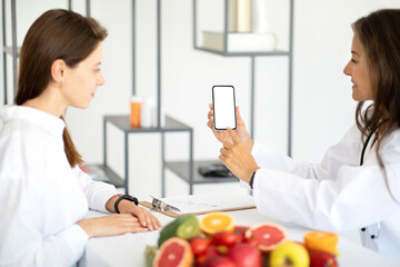 Happy european middle aged lady doctor nutritionist in white coat advises woman patient, recommends...
