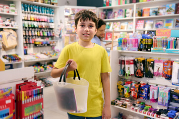 Handsome teenage schoolboy, smart student smiles at camera, standing with a shopping cart in the school stationery store