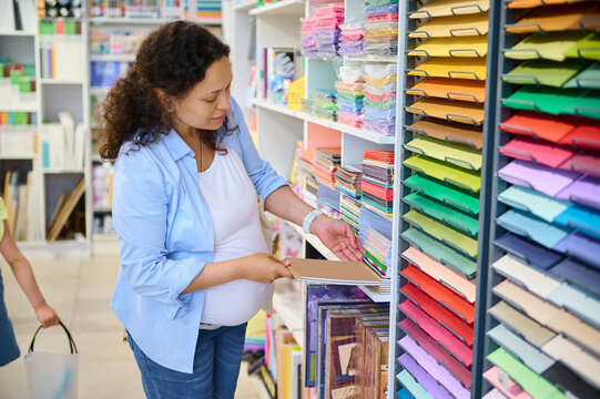 Attractive pregnant woman choosing color paper for design, pastel drawing or watercolor painting in art stationary shop
